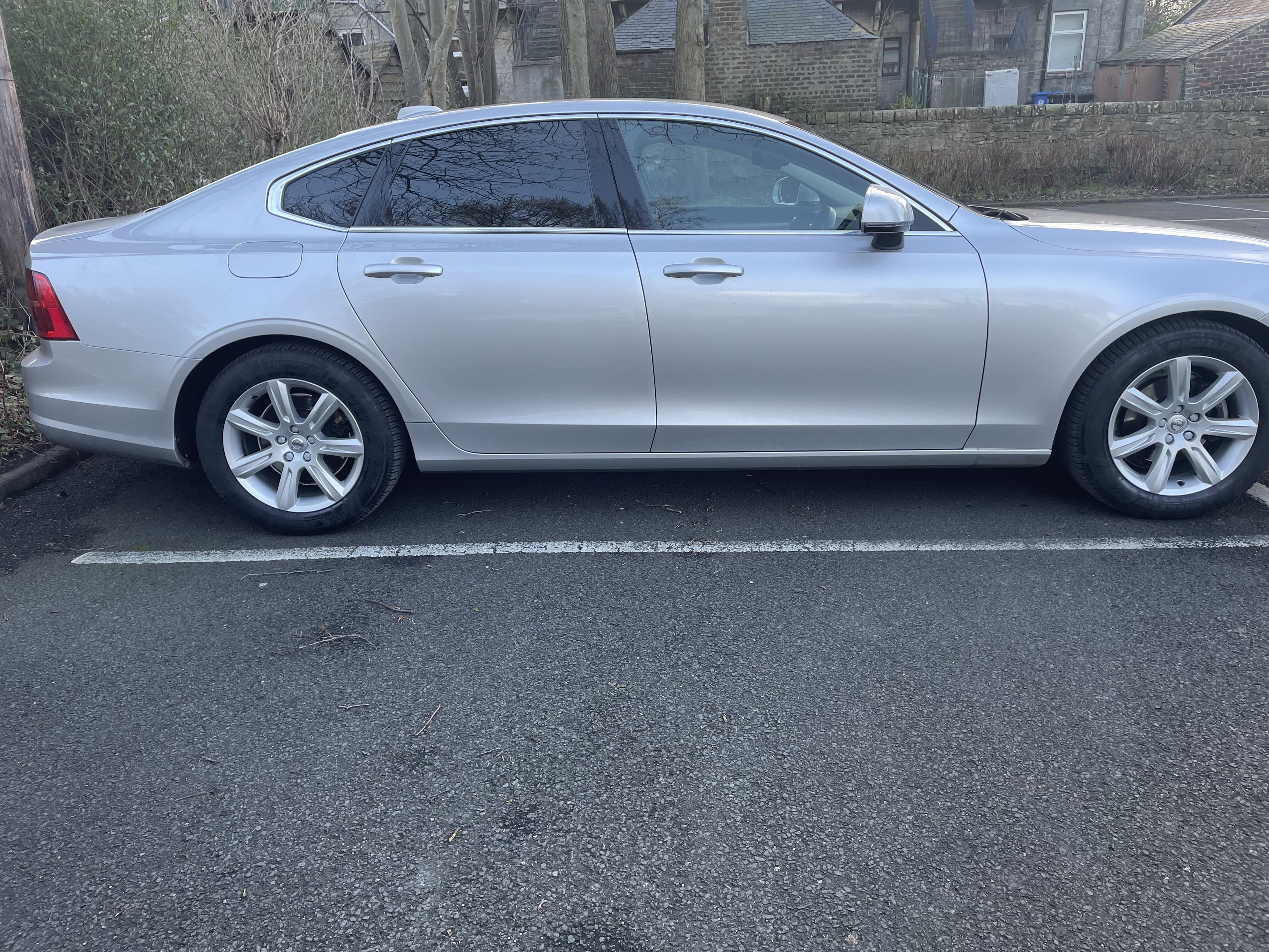 Silver Volvo S90 executive saloon parked on a quiet street, side profile view